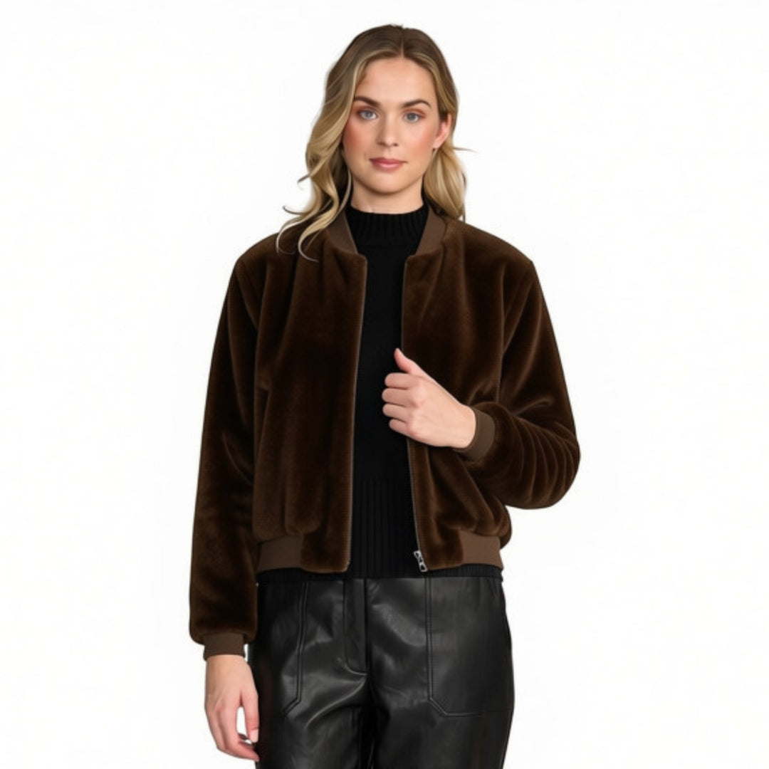 A woman modelling a dark brown faux fur bomber jacket over a black ribbed turtleneck and black faux-leather pants, shot against a solid white background.