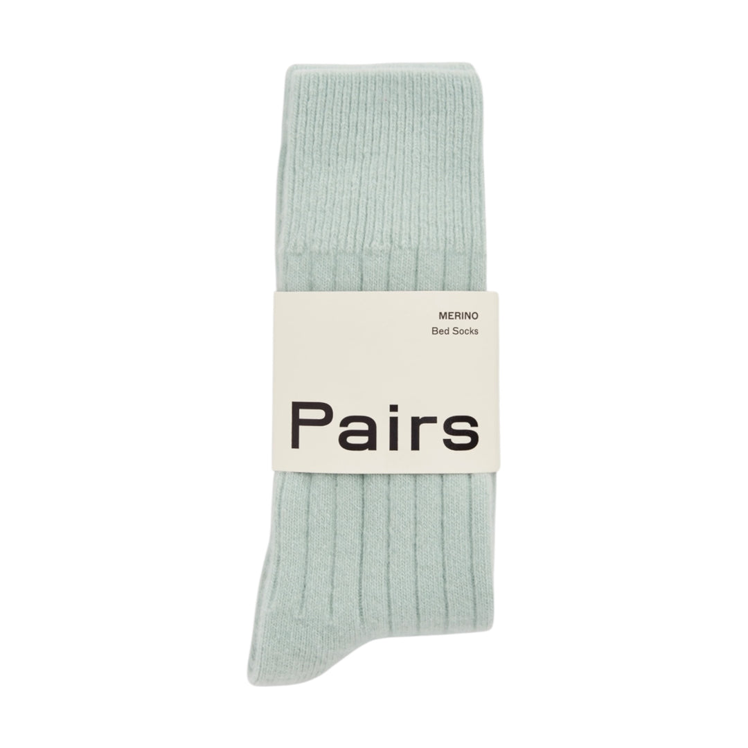 A pair of ribbed bed socks in a pale mint green color, wrapped with a white paper band that reads 'Pairs' and 'MERINO Bed Socks'.