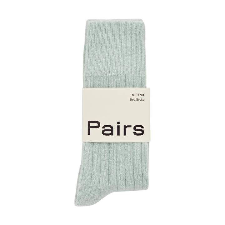 A pair of ribbed bed socks in a pale mint green color, wrapped with a white paper band that reads 'Pairs' and 'MERINO Bed Socks'.